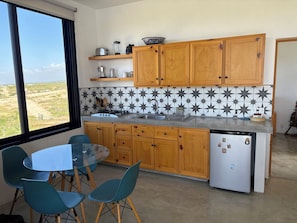 A kitchen with wooden cabinets, a white refrigerator, a sink, and a dining area with a glass table and chairs. - One bedroom casita with pool and ocean views (Todos Santos)