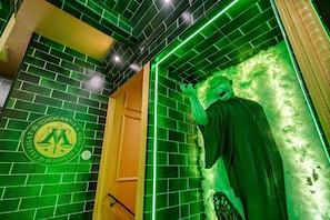 Ein Zimmer mit grün gefliesten Wänden, einer Statue und einer Tür mit einem runden Wappen.