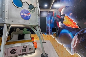 Ein raumschiff-thematisches Zimmer mit NASA-Logo, einer Raumfähren-Mural und einem Bett im Weltraumdesign.