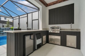 Una cuina exterior moderna amb una barbacoa integrada, un frigorífic i un rentaplat.