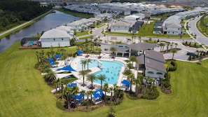 An aerial view of a residential area with a large swimming pool surrounded by houses, palm trees, and a river. - Your New 9BR Upscale Orlando Getaway (2576SN) (Kissimmee)
