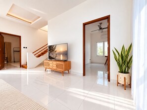 Una sala de estar moderna con un televisor de pantalla plana, un mueble de madera, una escalera y una planta en maceta.
