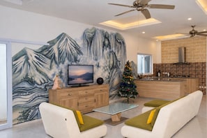 A modern living room with a TV, a Christmas tree, and a kitchen in the background. - 3BR Victoria Jimbaran Villa with Pool (Jimbaran)