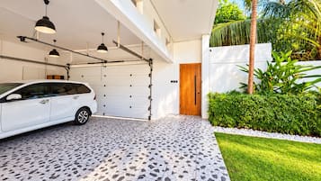 A modern garage with a white car parked inside, a tiled floor, and a wooden door.