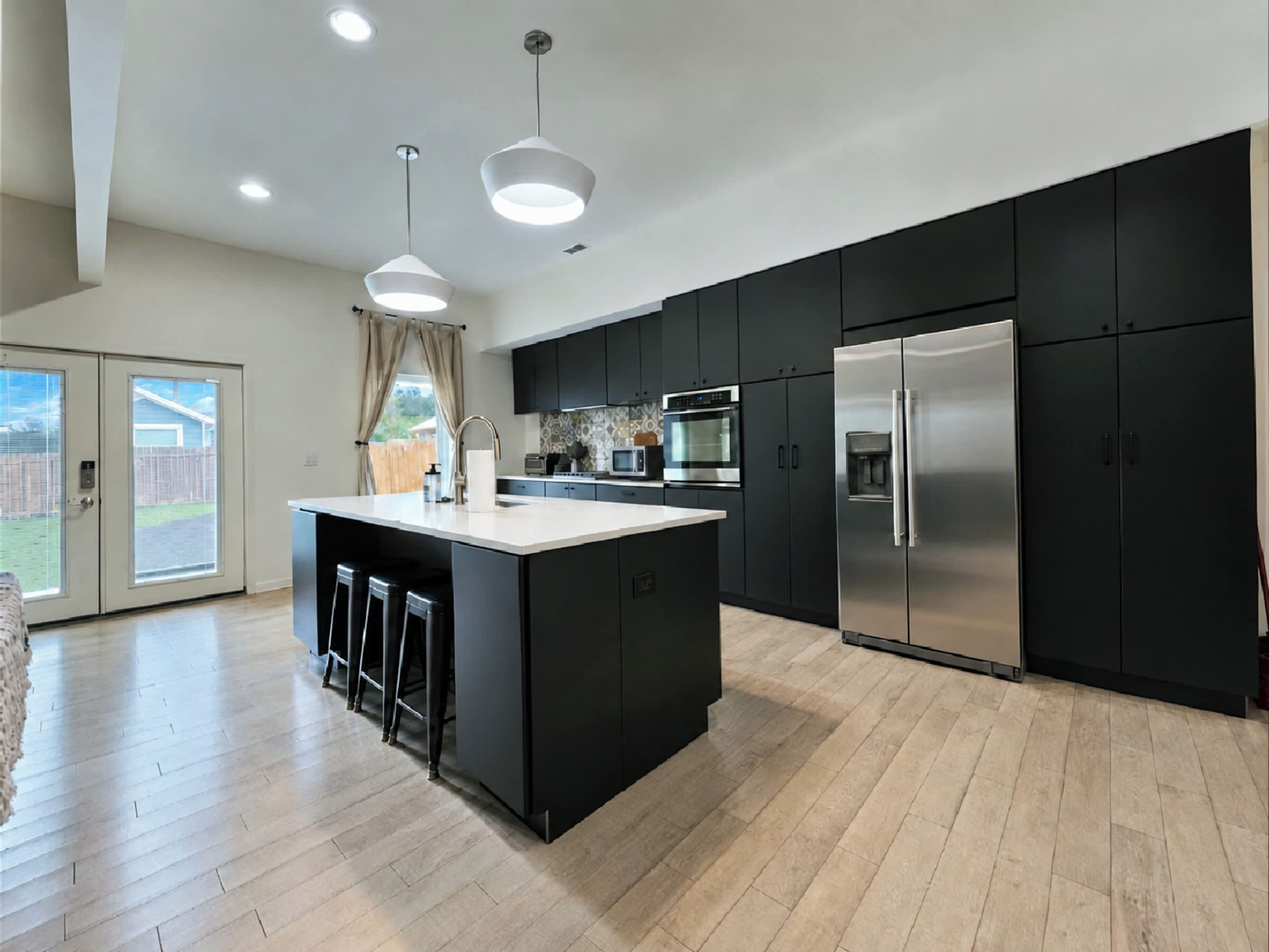 A modern kitchen with a central island, black cabinetry, stainless steel appliances, and a large window.