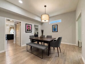 A dining area with a wooden table, grey chairs, a bench, and a pendant light. - Fountain Square 3BR 2 Kings Sleeps 8 (Indianapolis)