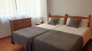 A double bed with two pillows, a wooden nightstand, a dresser, and a window with curtains. - 2A Apartamentos Latin SilHouse Nerja (Nerja)