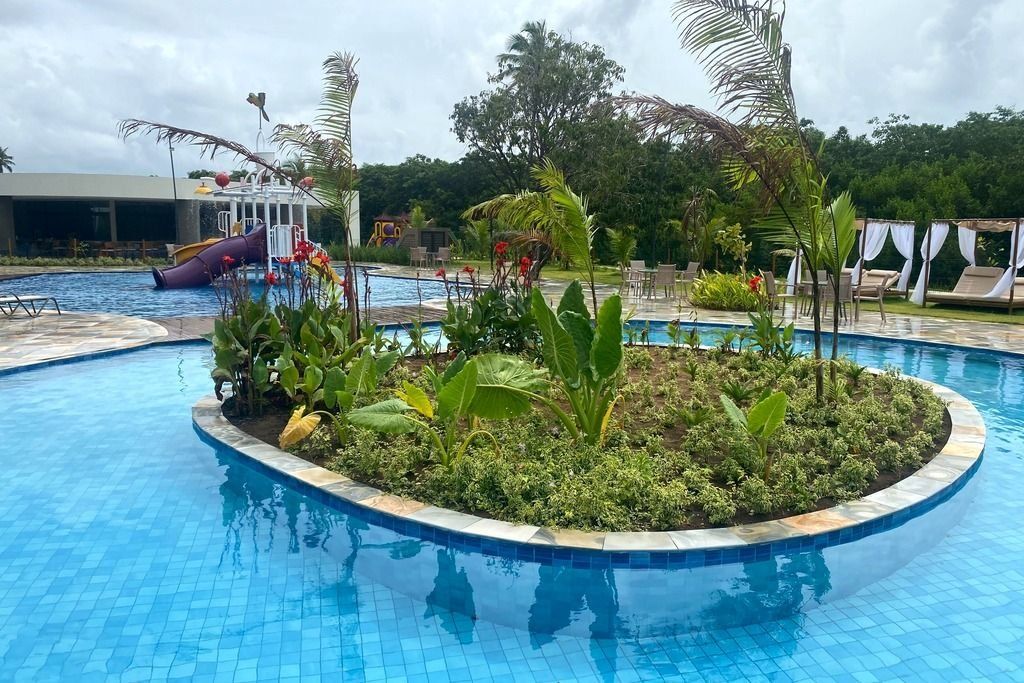 Una piscina con tobogán de agua, rodeada de exuberante follaje y sillas de descanso.