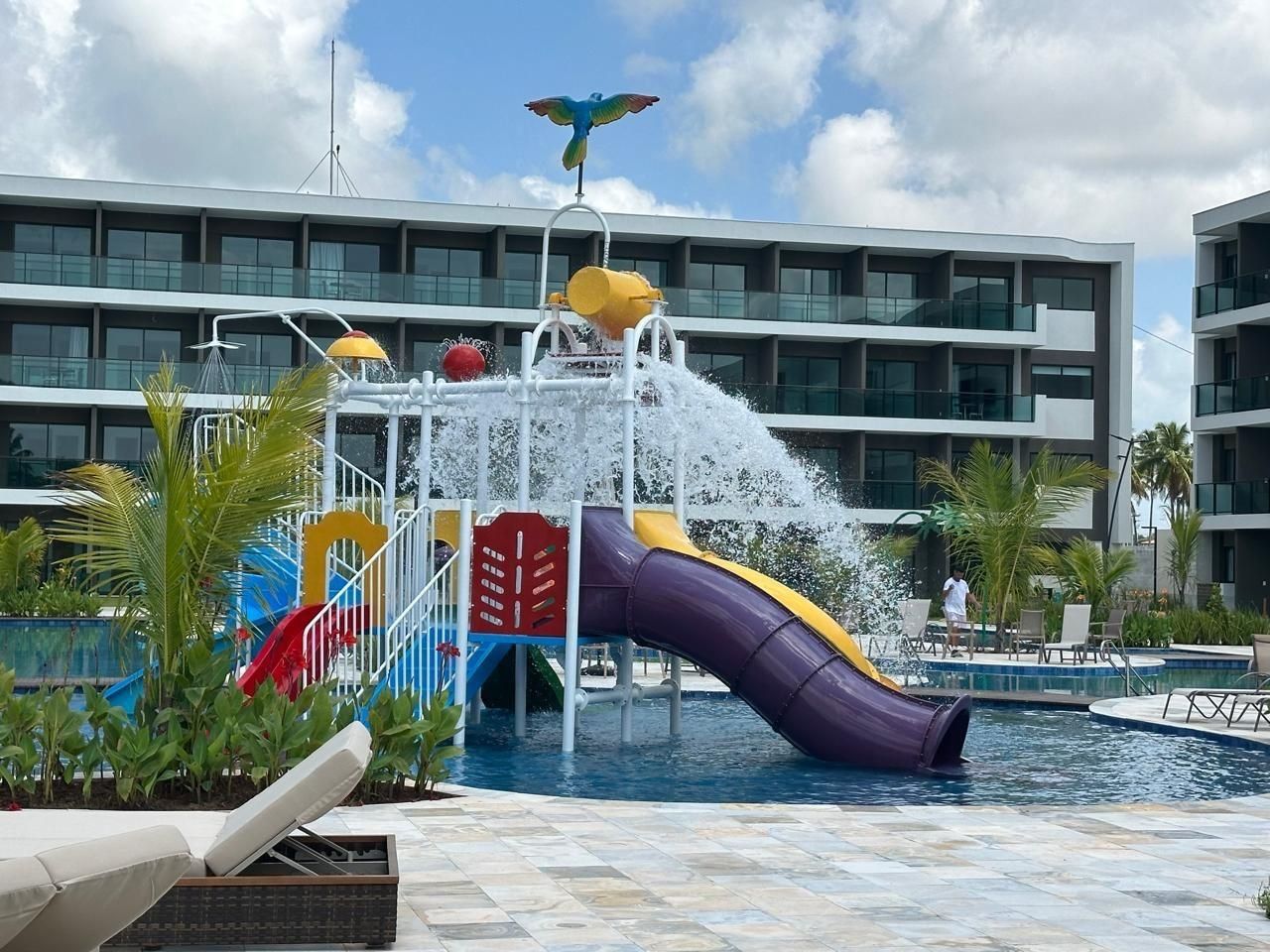 A water park with a slide, a pool, and a building with balconies in the background.