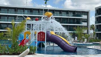 Parque acuático con tobogán, piscina y un edificio con balcones al fondo.