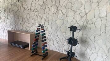 Una habitación con piso de madera, pared de piedra, un banco y dos estaciones de levantamiento de pesas.