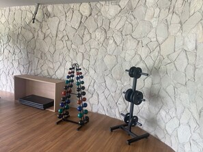 A room with a wooden floor, a stone wall, a bench, and two weightlifting stations.