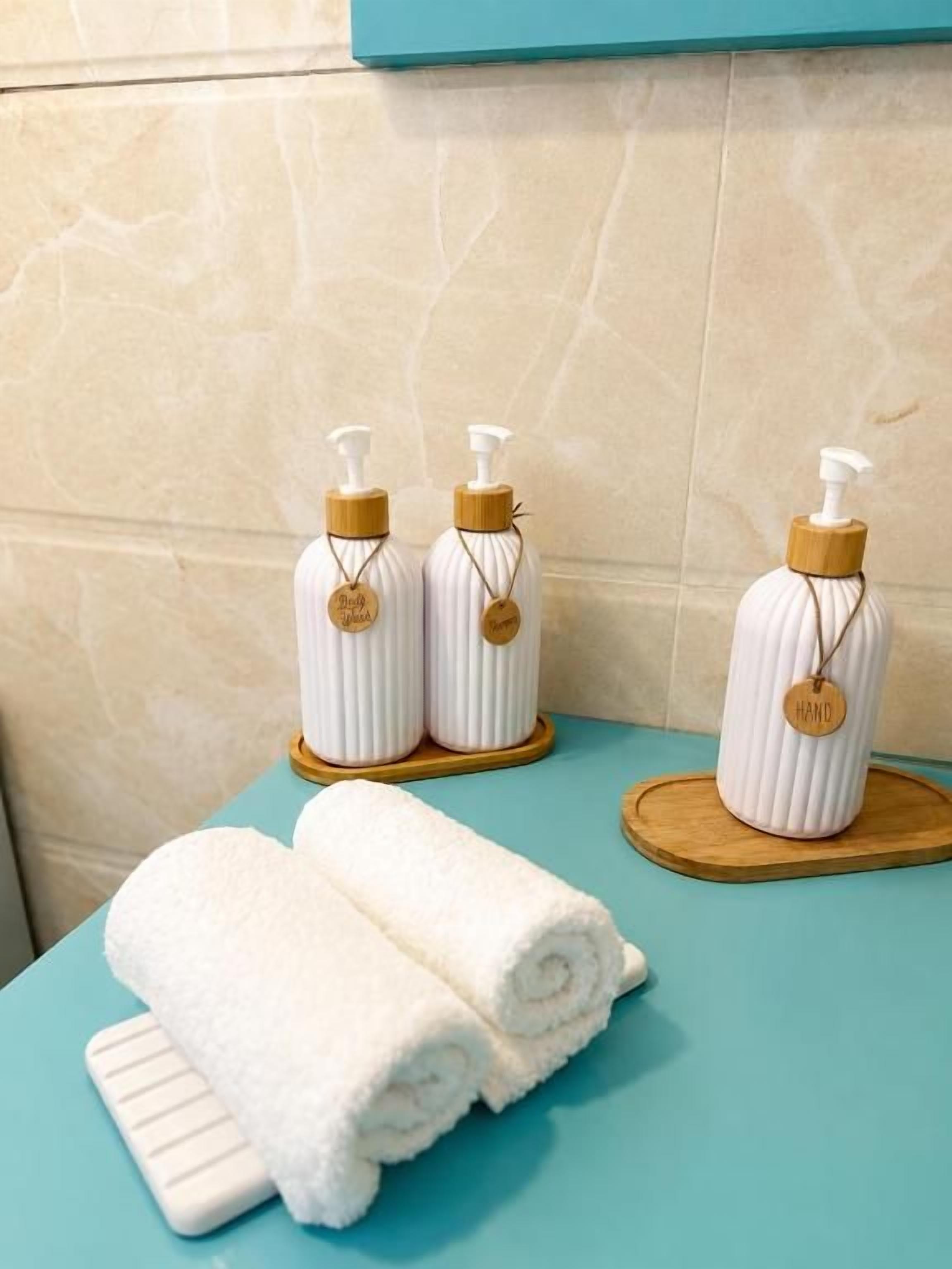 A bathroom with two white towels on a blue surface, two white soap dispensers on wooden stands, and a white bottle with a wooden cap on a wooden tray.