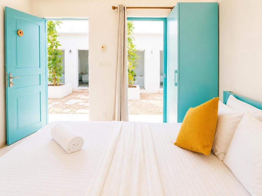 A hotel room with a bed, a yellow pillow, and a view of an outdoor area with plants.