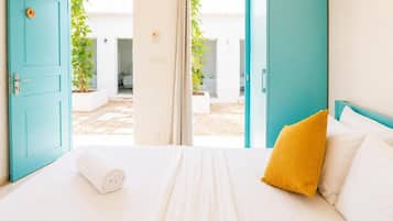 A hotel room with a bed, a yellow pillow, and a view of an outdoor area with plants.