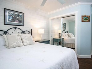 Een slaapkamer met een bed, nachtkastje, spiegel en een lijst met een foto aan de muur.