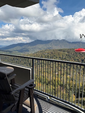 A balcony with a table and chairs, overlooking a mountainous landscape with a red umbrella. - Updated 6th -Floor Condo with Stunning Panoramic Grandfather Mountain View’s (Sugar Mountain)
