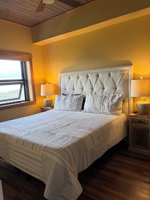 A bedroom with a large bed, two bedside lamps, a wooden nightstand, and a window with a view. - Updated 6th -Floor Condo with Stunning Panoramic Grandfather Mountain View’s (Sugar Mountain)
