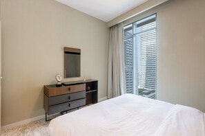 A hotel room with a bed, a dresser, a mirror, and a window with blinds. - Sea & Marina View 2BR | Private Beach & Pool (Dubai)