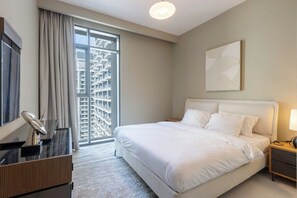 A hotel room with a bed, a desk, a chair, a lamp, a painting, and a large window with a view of buildings. - Sea & Marina View 2BR | Private Beach & Pool (Dubai)