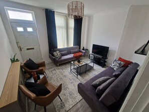 Una sala de estar con sofá, sillón, mesa de centro y televisor.