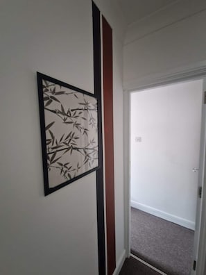Ein Flur mit einem gerahmten Kunstwerk an der Wand, einer Tür am Ende und einem Teppichboden.