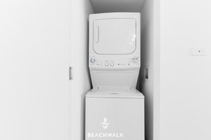 A white washing machine with a control panel, located in a narrow space between two white walls. - Stylish 1BR APT - Resort‑Style experience (Hallandale Beach)