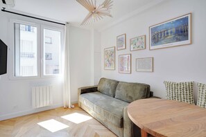 A modern living room with a sofa, a dining table, and a large window. - Cosy & Modern Apartment in Montreuil - 1br/ 4P (Montreuil)