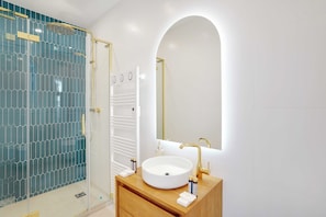A modern bathroom with a glass-enclosed shower, a white sink with gold fixtures, and a large mirror. - Cosy & Modern Apartment in Montreuil - 1br/ 4P (Montreuil)