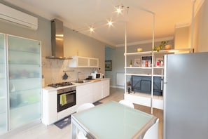 A modern kitchen with white cabinetry, a gas stove, a built-in oven, and a microwave. There is a dining table with chairs, and a refrigerator is visible in the corner. - Fabio's Guest House & Parking (Firenze)