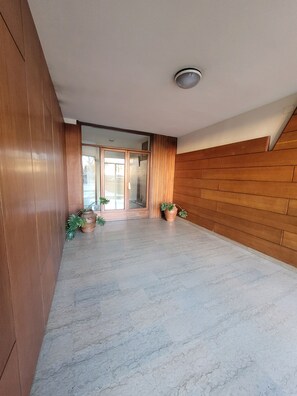 A spacious hallway with wooden paneling on the walls and a marble floor. There are two potted plants and a glass door leading to another room. - Fabio's Guest House & Parking (Firenze)