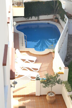 A rooftop swimming pool with a curved edge, surrounded by a white wall and a small garden area with potted plants. - 2C Apartamentos Latin SilHouse Nerja (Nerja)