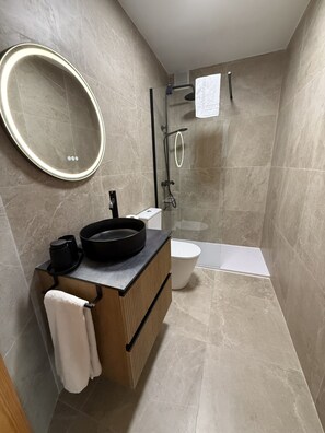 A modern bathroom with a round mirror, a black sink, a toilet, and a shower area. - .2C Apartamentos Latin (Nerja)