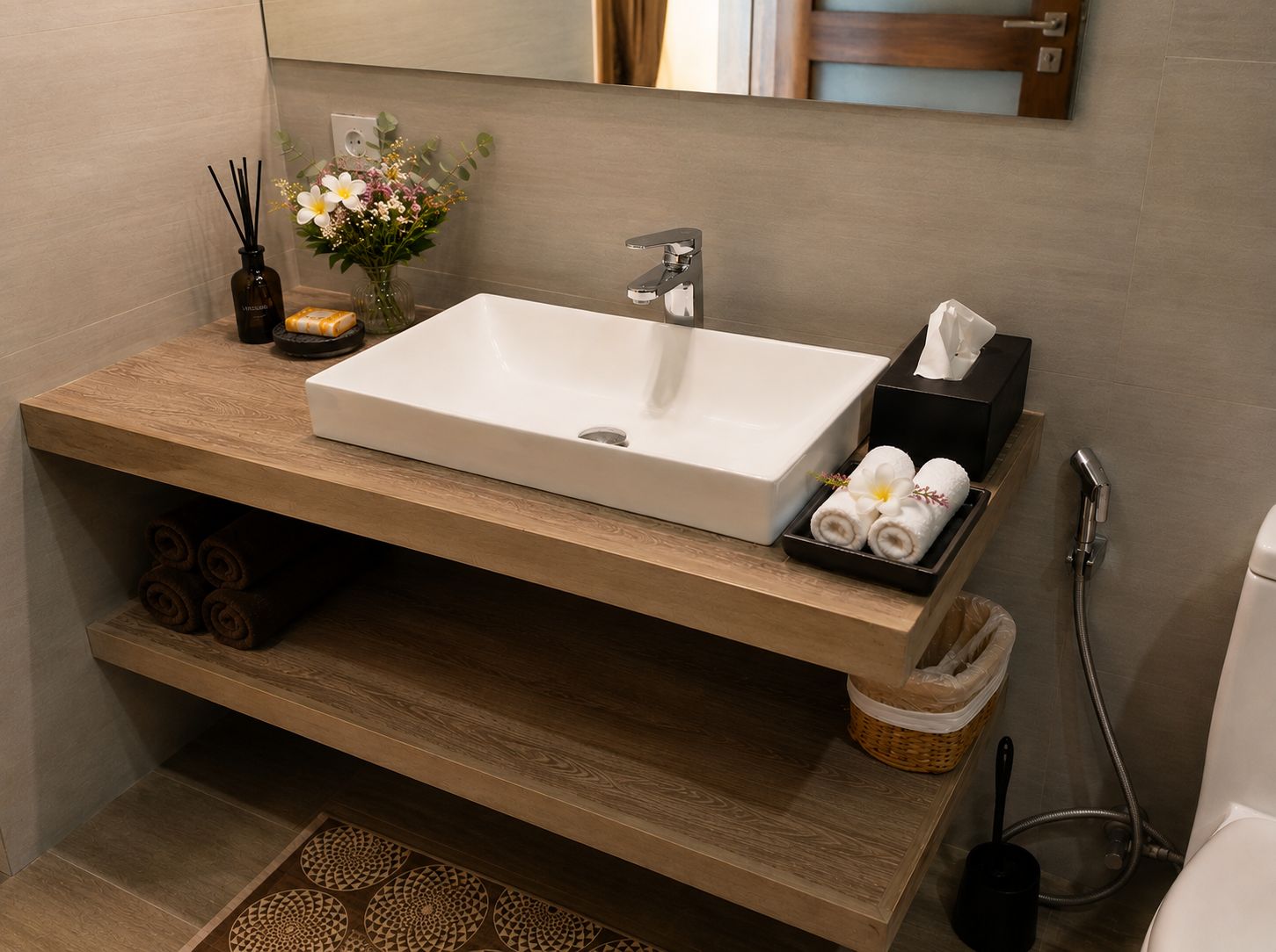 A bathroom with a rectangular sink, a towel rack, a soap dish, and a small vase with flowers.