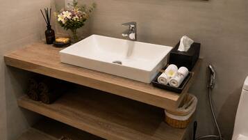 A bathroom with a rectangular sink, a towel rack, a soap dish, and a small vase with flowers.