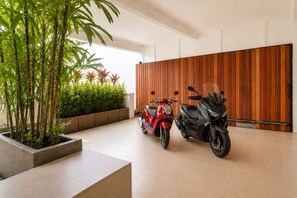 A clean, modern indoor space with two scooters parked near a wooden wall, a concrete planter with green plants, and a tiled floor. - 3BR New Luxury Villa Jimbaran/Nusa Dua (Badung)