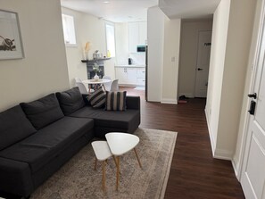 Ein modernes Wohnzimmer mit einem Ecksofa, einem kleinen weißen Tisch und einem gemusterten Teppich.