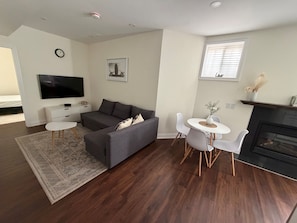 Ein modernes Wohnzimmer mit einem grauen Sofa, einem Flachbildfernseher, einem Esstisch mit Stühlen und einem Kamin.