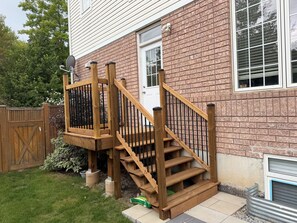 Eine Holztreppe führt zu einem Haus mit einer Ziegelaußenwand und einer weißen Tür.