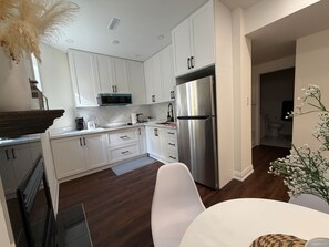 Una cocina moderna con armarios blancos, un refrigerador de acero inoxidable y una zona de comedor con una mesa y sillas blancas.
