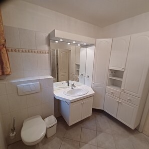 Ein Badezimmer mit Toilette, zwei Waschbecken, einem Spiegel und einem Schrank.
