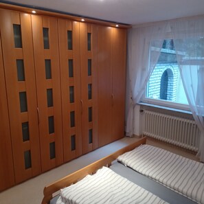 Et soveværelse med en stor garderobe, et vindue der viser udsigt til en murstensbygning, og en radiator.