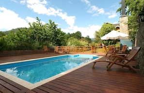 A rectangular swimming pool with a wooden deck, surrounded by lounge chairs and a wooden fence.