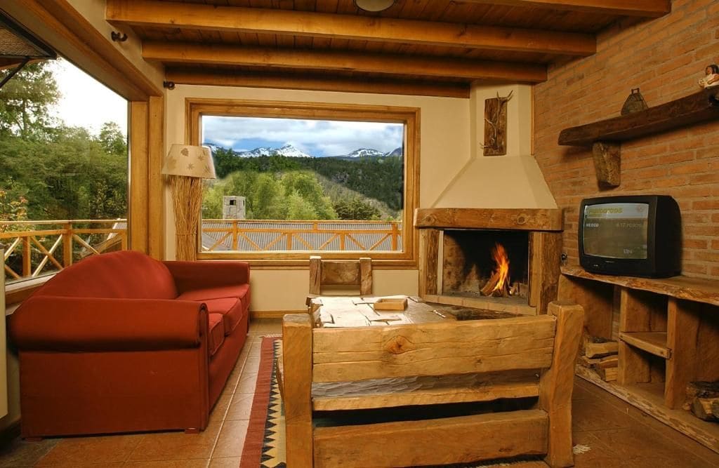Une pièce chaleureuse avec une cheminée, une télévision, un canapé et une vue sur un paysage montagneux, visible à travers une grande fenêtre.