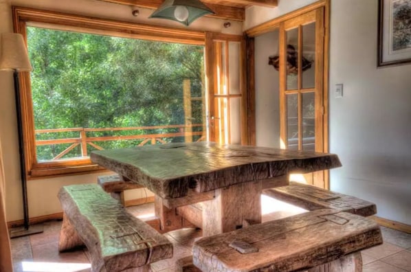 A rustic wooden table with benches in a room with a large window overlooking greenery.