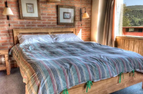 A bed with a striped blanket, a wooden headboard, and a brick wall with framed pictures.