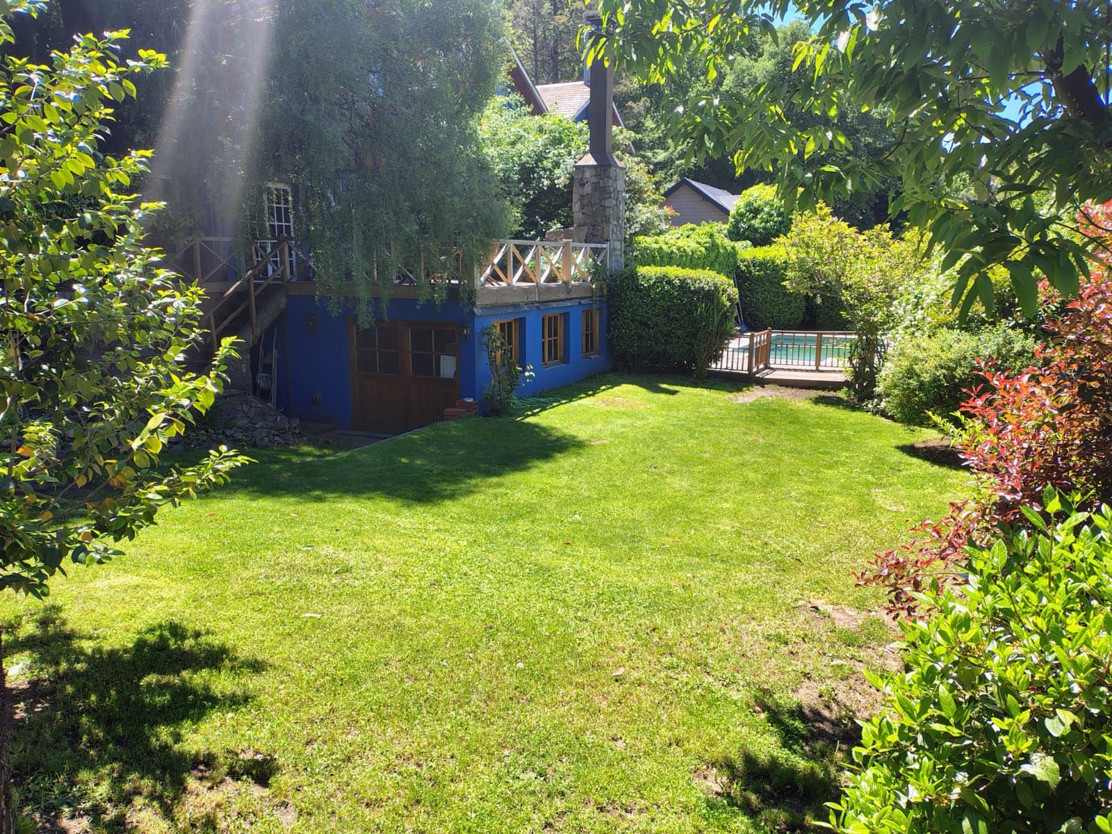 Un patio trasero con una casa azul, una terraza de madera y una piscina.