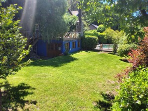 A backyard with a blue house, a wooden deck, and a swimming pool.