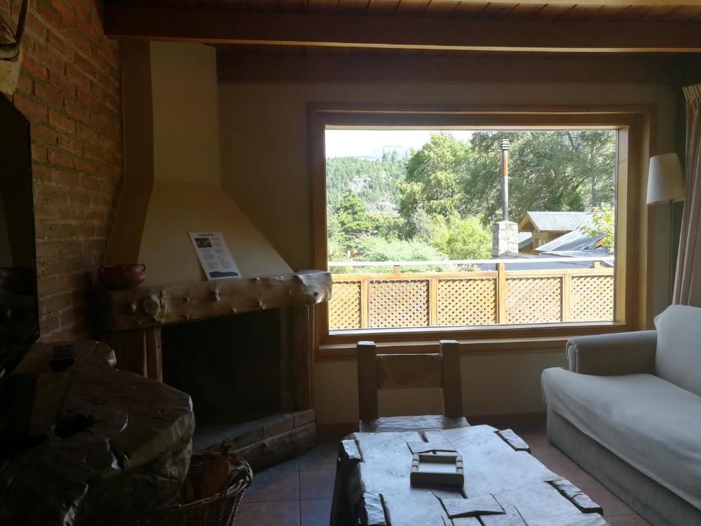 A cozy living room with a fireplace, a window with a view of greenery, and a white sofa.