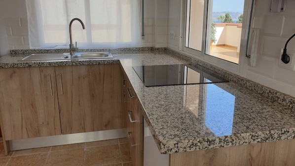 A kitchen with a granite countertop, stainless steel sink, and wooden cabinets. - Atico Apartamentos Latin (Nerja)